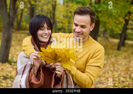 Glückliches Paar im Herbstpark mit gelben Blättern, in eine gemütliche Decke gehüllt Stockfoto