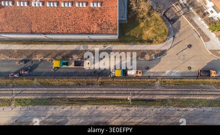 Ein Blick von oben auf den Straßenpflaster in Siska, Ljubljana. Schwere Walzen, Asphaltfertiger und Versorgungsfahrzeuge arbeiten in einer synchronisierten Linie neben einem Stockfoto