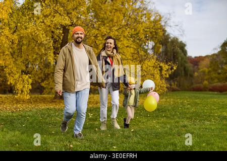 Glückliche Familie, die im Herbstpark läuft, Eltern und Kind mit bunten Ballons Stockfoto
