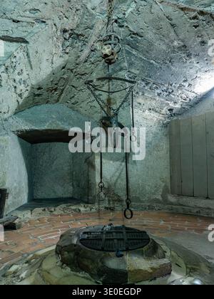 Mittelalterliches Foltergestell, das an Einer gewölbten Steindecke über Einem überdachten runden Dungeon-Brunnen in Einer dunklen Kammer, Prag, Tschechische Republik, hängt. Stockfoto