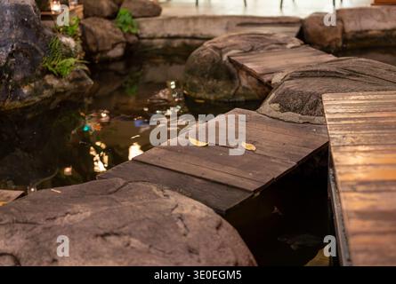 Kleiner Teich in der Nacht mit Holzsteg und zwei gelben Blättern auf dem Geländer. Ruhige dunkle Szene mit Reflexionen auf dem Wasser, die eine friedliche A erzeugen Stockfoto