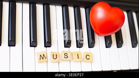 Wortkünstler aus Holzwürfeln auf einem S ynthesizer-Schlüssel auf schwarzem und weißem Hintergrund mit rotem Herzen. Klavieroktave aus nächster Nähe. Keyboard-Musical i Stockfoto
