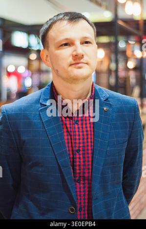 Porträt eines Mannes, der einen blauen Blazer und ein rotes kariertes Hemd trägt und nachdenklich wegschaut. Stockfoto