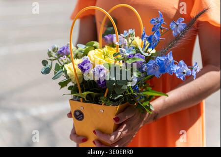 Junge Erwachsene Frau mit dekorativem Korb mit bunten frischen Blumen draußen im Sommerlicht. Festliches Geschenkkonzept mit Blumenmotiv für Hochzeiten und Feiern Stockfoto