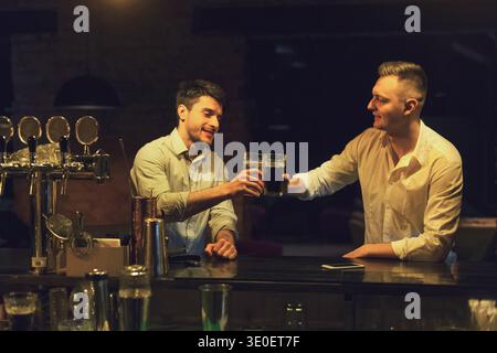 Zwei glückliche junge Männer reden und trinken Bier in der Bar Stockfoto