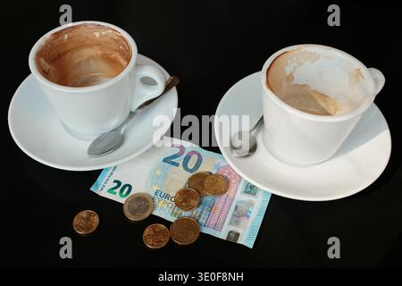 Zwei teilweise ausgetrunkene Cappuccino-Tassen mit Euro-Geldschein und Münzen auf dem Tisch. Konzept für die Bezahlung im Café für zwei Personen, Kaffeetreffen und soziale Ausgaben. Stockfoto