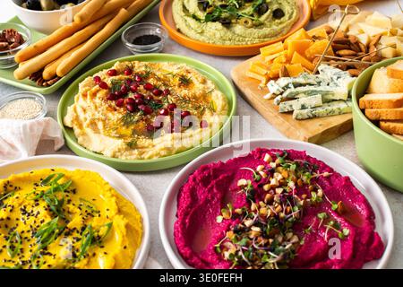 Ein lebhaftes Angebot zeigt verschiedene Arten von Hummus, darunter Klassik, Rote Bete, Brokkoli und Kurkuma. Begleitet von Oliven und Brotstäbchen lädt es zum Teilen und Genießen ein Stockfoto