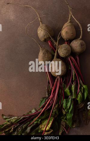 Rüben mit grünen Blättern ruhen auf einer braunen Oberfläche in einer Küche. Die Umgebung ist warm und gibt Hinweise auf frische Produkte, die zum Kochen oder Essen bereit sind Stockfoto