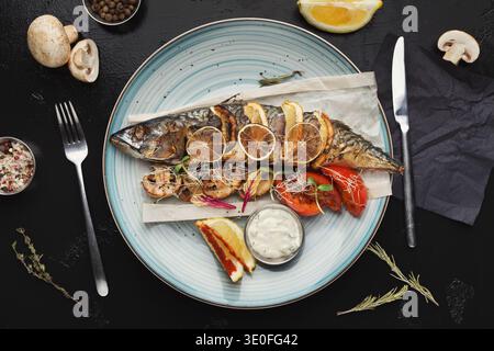 Gebratener Fisch mit Gemüse, serviert im Restaurant auf schwarzem Tisch Stockfoto