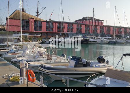 NH Collection Genua Marina. Genua, Italien. Modernes Hotel am Wasser mit rosa Fassade, das neben Yachten und Segelschiffen im Hafen liegt. Stockfoto