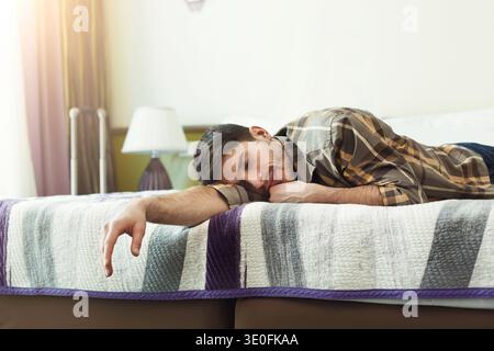 Der junge müde Mann schläft auf dem Bett im Hotelzimmer Stockfoto