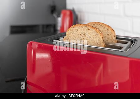 Brotscheiben in rotem Küchentoaster auf schwarzer Arbeitsplatte in moderner Wohnküche Stockfoto