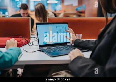 Geschäftsfrau präsentiert Daten während der Zusammenarbeit und Teamarbeit in einem modernen Open-Space-Büro auf einem Laptop-Bildschirm Stockfoto