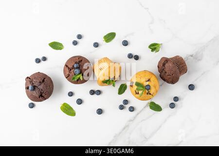 Frisch gebackene Muffins mit Schokoladenchips, Heidelbeeren und Minzblättern auf weißem Marmortischhintergrund. Schokoladen- und Bananenmuffins oder Cupcake c Stockfoto