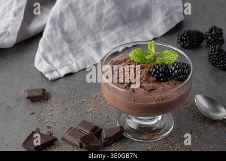 Kalter Kakao Kaffee Milch Dessert in Glasschale mit Minzblättern, Heidelbeere, Schokoladenbrösel und Stücke auf dunklem Steintisch Hintergrund. Schokoladenmokka Stockfoto