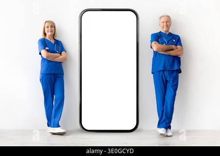 Zwei erfahrene Ärzte stehen neben einem großen Smartphone-Modell im Studio Stockfoto