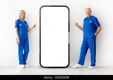 Zwei erfahrene Ärzte stehen neben dem Smartphone-Modell und zeigen auf einen leeren Bildschirm Stockfoto