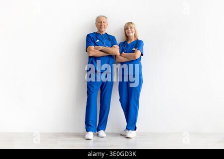 Reife Ärztinnen und Ärzte tragen blaue Peelings und stehen mit überkreuzten Armen Stockfoto