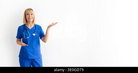 Senior weibliche Gesundheitsberaterin in blauen Peelings, die mit einer offenen Handfläche Gesten Stockfoto