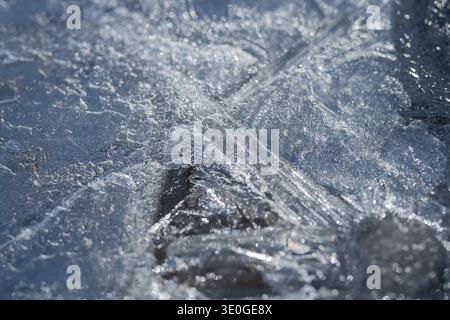 Naheis im Frühjahr mit dreieckigem Stein und glänzenden Kristallen, kühlen Blautönen, radialen Rissen, sonnendurchfluteten Highlights und subtilem Schmelzwasser Stockfoto