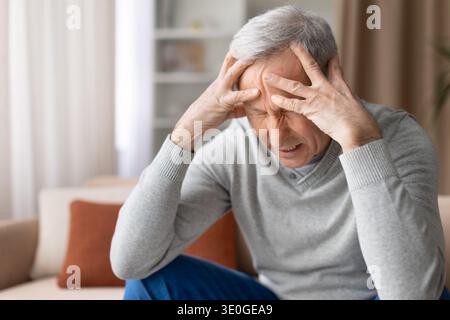 Gestresster Senior Mann, der zu Hause auf der Couch sitzt und den Kopf mit den Händen hält Stockfoto
