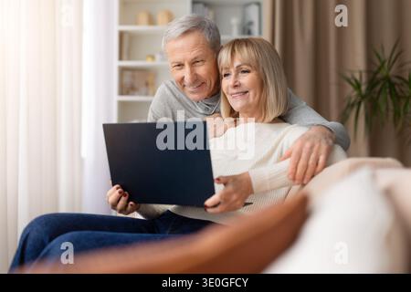 Seniorenpaar, das zu Hause zusammen auf dem Sofa sitzt und einen Laptop benutzt Stockfoto