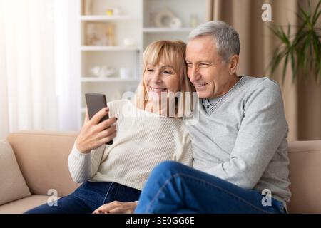 Seniorenpaar, das auf dem Sofa sitzt und Selfie mit Smartphone macht Stockfoto