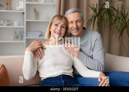 Reifes Paar posiert zusammen auf der Couch zu Hause und lächelt in die Kamera Stockfoto
