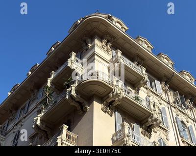 Verzierte Eckfassade des Wohngebäudes in La Spezia, Italien. Italienische Architektur mit dekorativen Stuckkonsolen und schmiedeeisernen Balkonen aga Stockfoto