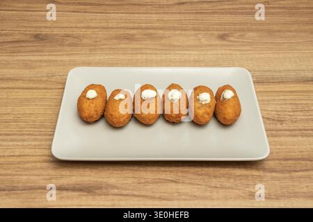 Eine Platte mit Kroketten in verschiedenen Geschmacksrichtungen: Etwas Schinken, etwas Huhn und etwas Käse, alle paniert und frittiert, bereit für ein Familienessen. Stockfoto