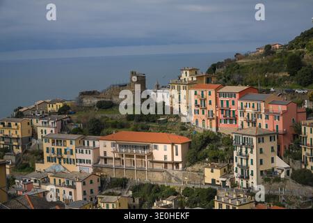 Riomaggiore, Cinque Terre. Farbenfrohe ligurische Häuser kaskadieren einen steilen Hügel hinunter in Richtung Mittelmeer unter einem historischen Turm mit sichtbarem Klo Stockfoto