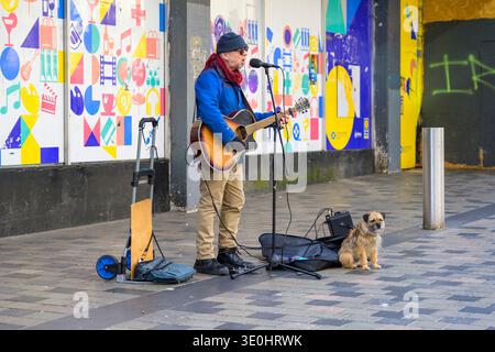 Ein Mann, der mit seinem Hund unterwegs ist, singt und Gitarre spielt, und auf der Sauchiehall Street, Glasgow, Schottland, Großbritannien zusieht Stockfoto