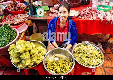 Eine lächelnde Frau verkauft frisches Obst, Gemüse und Fleisch auf einem Markt in Phnom Penh, Kambodscha während der geschäftigen Tageszeiten. Stockfoto