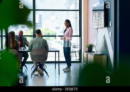 Junge Geschäftsfrau leitet Team-Meeting in einem modernen Büro mit Fenstern tagsüber Stockfoto