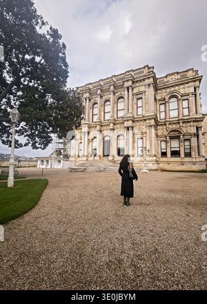 Eine Frau im dunklen Mantel, die die üppigen Gärten und die große architektonische Fassade des historischen Beylerbeyi Palace an der Bosporus-Küste erkundet. Stockfoto