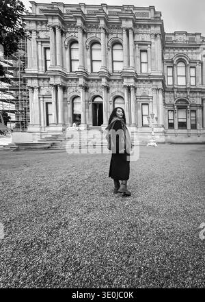 Ein dynamisches Schwarz-weiß-Foto einer Frau im Wintermantel, die zurückblickt und die Gärten und die große architektonische Fassade des Beylerbeyi Pala erkundet Stockfoto