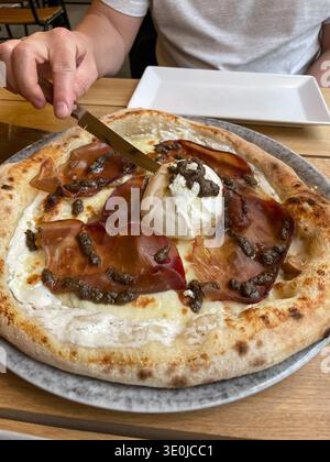 Handgeschnittene Pizza mit Burrata, Trüffel und Schinken auf knuspriger gebackener Kruste, serviert auf Tellern im Restaurant. Restaurantmarketing Stockfoto