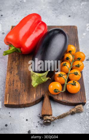 Frisches Gemüse auf hölzernem Schneidebrett über hellem texturiertem Hintergrund mit Kopierraum, roter Paprika Auberginen und Kirschtomaten. Stockfoto