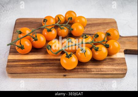 Gelbe Kirschtomaten auf Weinrebe auf hölzernem Schneidebrett über hellem texturiertem Hintergrund mit Kopierraum, frische Bio-Produkte. Stockfoto