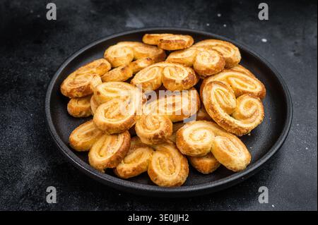 Klassische französische palmier-Kekse aus Blätterteig in schwarzer Schüssel dunkler Hintergrund süß gebackenes Dessert-Konzept. Stockfoto