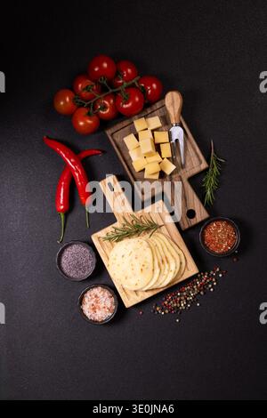Vorspeise mit verschiedenen in Scheiben geschnittenen und in Würfel geschnittenen Käsesorten, frischen Tomaten, roten Chili, Rosmarin und verschiedenen Gewürzen Stockfoto