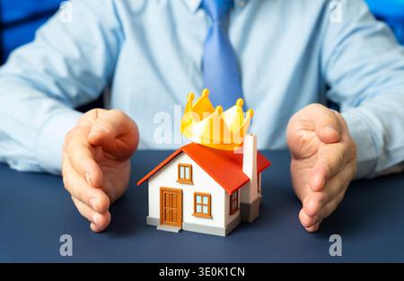 Ein Mann fesselt seine Hände um ein Haus mit einer Krone auf dem Dach. Sachversicherung und Schutz wertvoller Häuser. Premium-Wohnungen, Kauf und Rentabilität Stockfoto