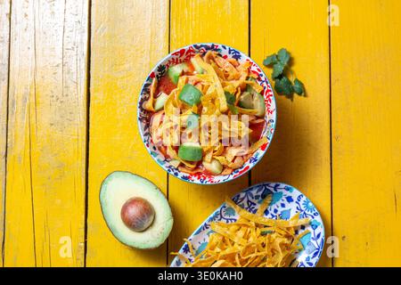 Tortilla frittierte aztekische Suppe mit frischen Zutaten auf einem leuchtend gelben Tisch Stockfoto