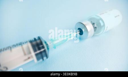 Nahaufnahme der Spritzennadel, Aufziehen des Impfstoffes aus der Durchstechflasche auf blauem Hintergrund, der die Impfung und das pharmazeutische Arzneimittel darstellt Stockfoto