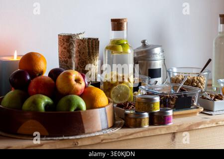 Der Holztisch in einem Wellness-Rückzugsbereich bietet eine Vielzahl von Frühstücksartikeln. Eine Holzschale bietet Platz für verschiedene Äpfel, Orangen und Pflaumen. In der Nähe Stockfoto