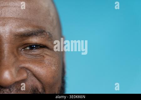 Afroamerikaner, der sanft lächelt, während er im Studio vor türkisfarbenem Hintergrund posiert Stockfoto