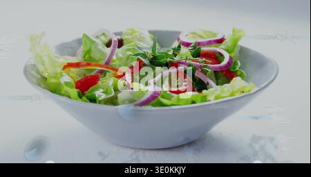 Mit weißer Keramikschale mit Salat, roter Paprika, Tomatenhälften und Kräuterzweigen auf der Tischplatte Stockfoto