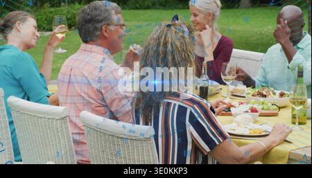 Sechs Erwachsene unterhalten sich auf dem Rasen, mit Weinflaschen aus gelbem Tuch, Käseblau Stockfoto