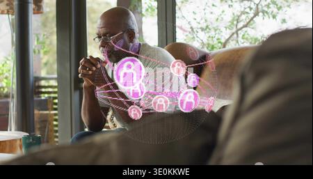 Sitzender älterer Mann mit Brille, grauem Hemd auf dem Sofa zu Hause, mit rosa lila Hologrammknoten Stockfoto
