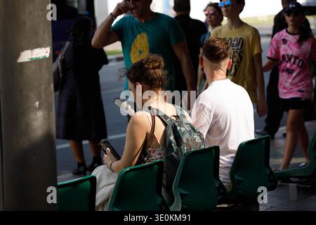 BANGKOK, THAILAND-22. Februar 2026: Touristenpaar wartet auf Bus und Smartphone, persönlicher Moment mit Telefon, Rückansicht, Maha Rat Road. Stockfoto